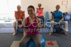 Front view of senior people exercising with female trainer using dumbbells
