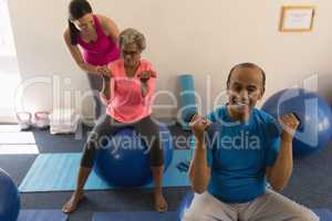 Female trainer assisting senior woman in fitness studio