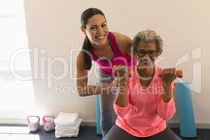 Front view of female trainer assisting senior woman in fitness studio
