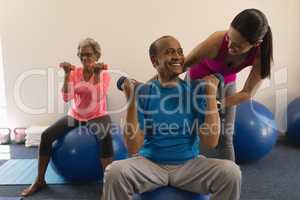 Front view of female trainer assisting senior man in fitness studio