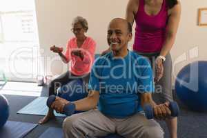 Female trainer assisting senior man in fitness studio