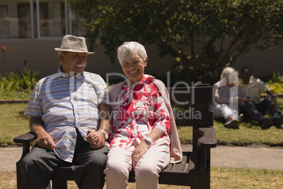 Front view of senior couple holding hands and sitting on bench in garden