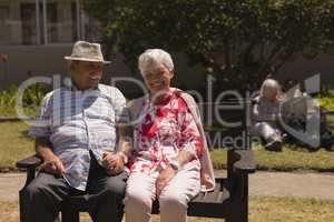 Front view of senior couple holding hands and sitting on bench in garden