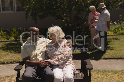 Front view of senior couple holding hands and sitting on bench in garden