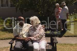 Front view of senior couple holding hands and sitting on bench in garden