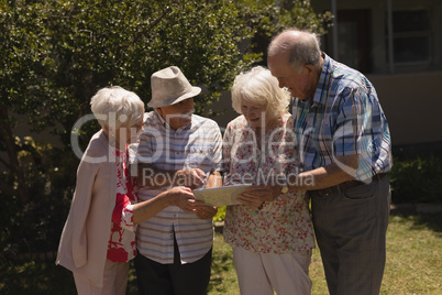 Front view of senior friends discussing over digital tablet in garden