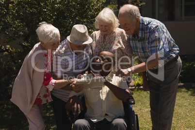 Front view of senior friends discussing over digital tablet in garden
