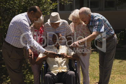 Front view of senior friends reviewing photos on mobile phone in garden