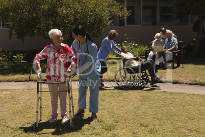 Young female doctor helping disabled senior woman in garden