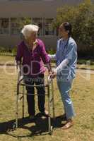 Young female doctor helping disabled senior woman in garden
