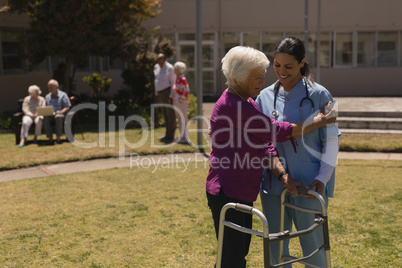 Young female doctor helping disabled senior woman in garden