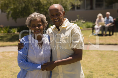 Front view of senior couple holding hands and looking at camera in garden