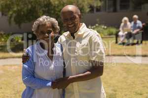 Front view of senior couple holding hands and looking at camera in garden