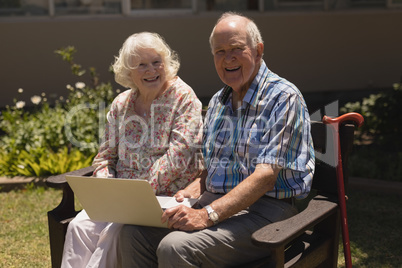 Front view of senior couple with laptop looking at camera in garden