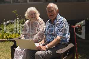 Front view of senior couple with laptop looking at camera in garden
