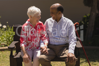 Front view of senior couple sitting on bench and looking each other in garden