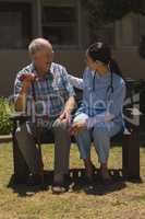 Young female doctor talking with senior man while sitting on bench
