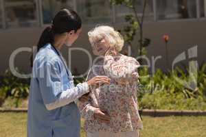 young female doctor examining senior woman in garden