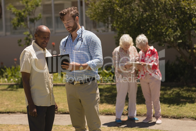 Male doctor interacting with senior man over clipboard