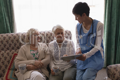 Female doctor and senior women discussing over digital tablet in living room