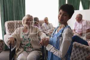Female doctor holding hands of disabled senior woman in living room