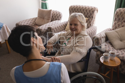 Female doctor interacting with disabled senior woman in living room