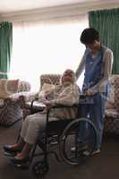 Female doctor interacting with disabled senior woman in living room