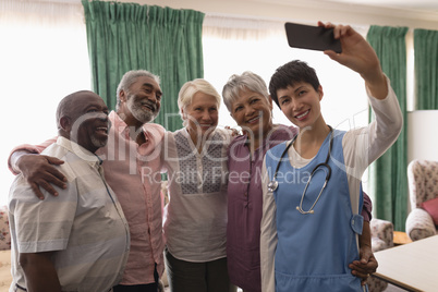 Senior people and female doctor taking selfie with mobile phone in living room