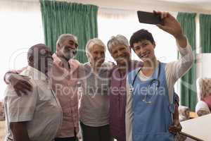 Senior people and female doctor taking selfie with mobile phone in living room