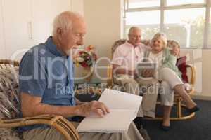 Blind senior man reading a braille book while senior couple using digital tablet at nursing home