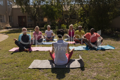 Female trainer training senior people in performing yoga