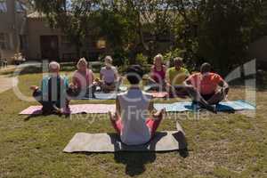 Female trainer training senior people in performing yoga