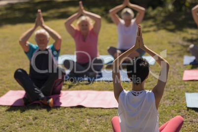 Female trainer training senior people in performing yoga