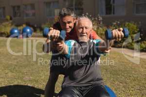 Trainer assisting senior man in performing exercise with dumbbells