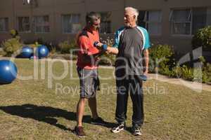 Trainer assisting senior man in performing exercise with dumbbells