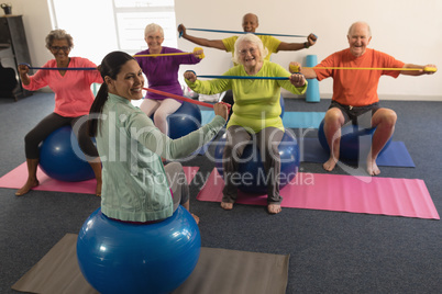 Young female trainer and senior people exercising with resistance band