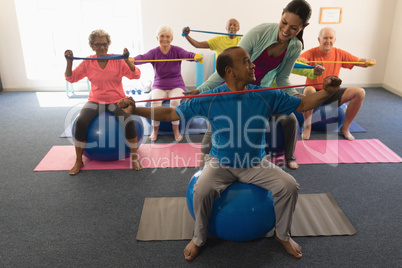 Young female trainer assisting senior man in fitness studio