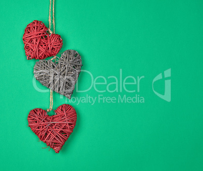 three wicker hearts hang on a rope, green background
