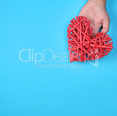 wooden wicker red heart in a female hand on a blue background
