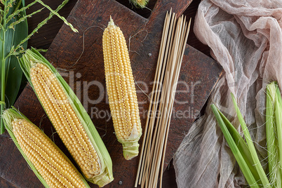 fresh ripe corn cobs on a brown wooden board