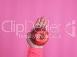 red ripe apple in a female hand on a pink background