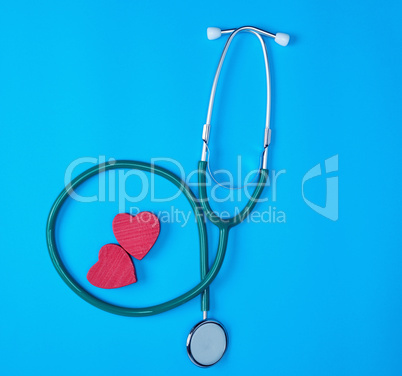 green medical stethoscope and two red wooden hearts