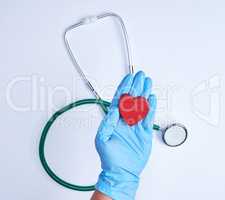 human hand with blue sterile gloves holding a red heart