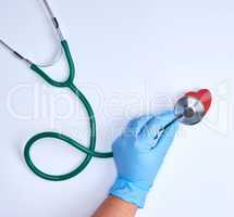human hand in blue sterile gloves holding a green stethoscope