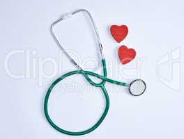 green medical stethoscope and two red wooden hearts