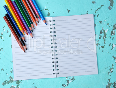 open notebook in a line and multi-colored wooden pencils