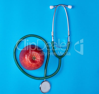 green medical stethoscope and ripe red apple