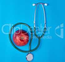 green medical stethoscope and ripe red apple