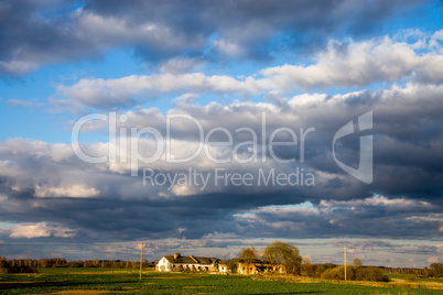 Landscape with cereal field, old farm house and blue sky.