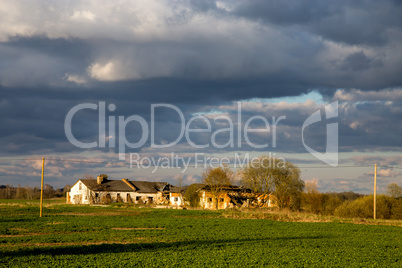 Landscape with cereal field, old farm house and blue sky.